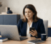 Contadora usando notebook e celular em escritório de contabilidade, consultando sistema do governo para representar cliente